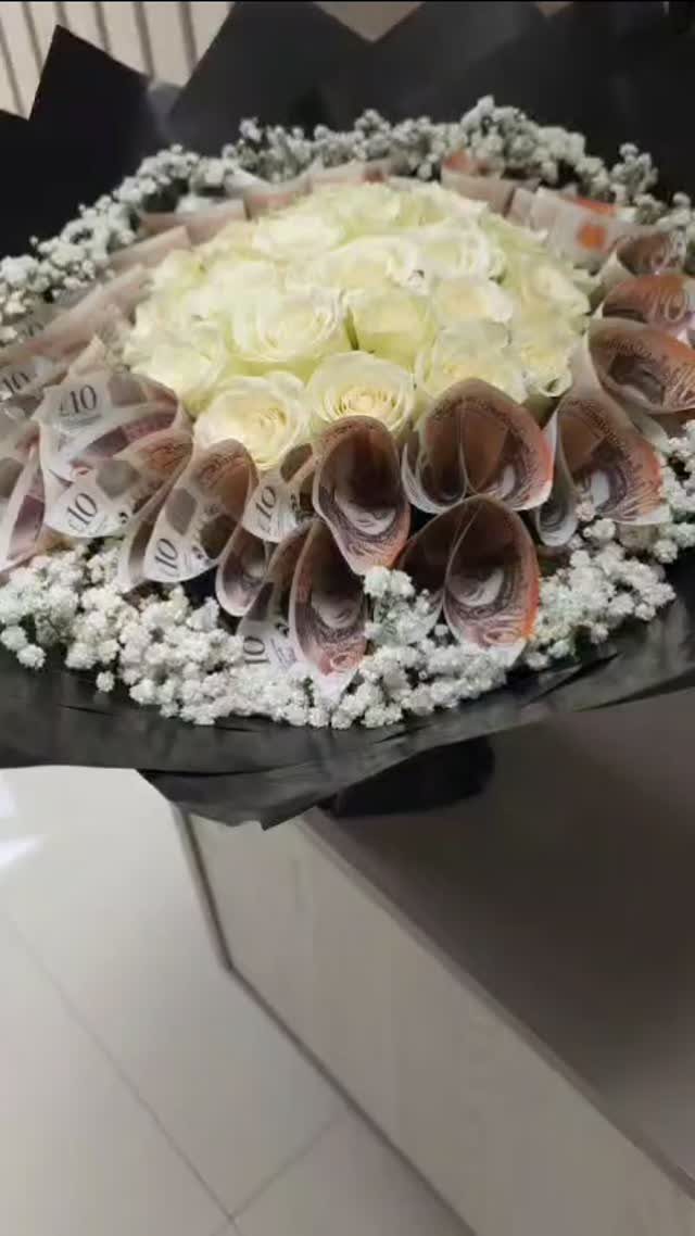 Bouquet of white roses and rolled banknotes accented with white baby's breath flowers.