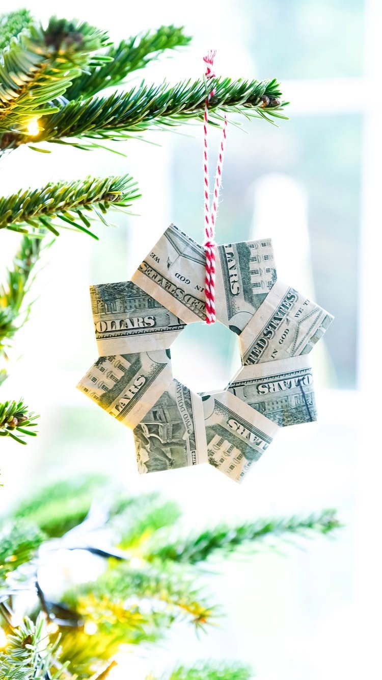 Folded dollar bill ornament hanging from a green Christmas tree branch by string.