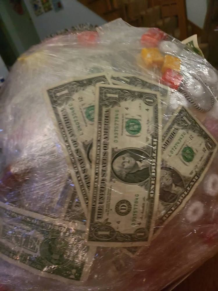 Saran wrap ball filled with one-dollar bills and colorful candies for a gift.