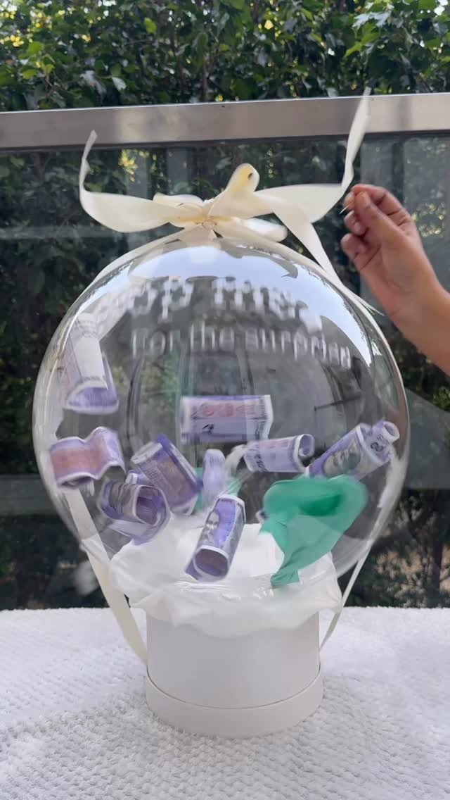 Clear balloon filled with rolled purple money bills on a white base.