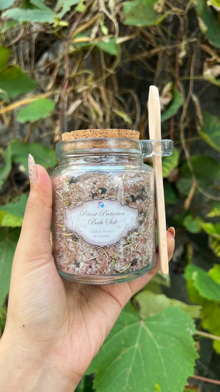 Glass jar of pink bath salts with a wooden spoon held against greenery