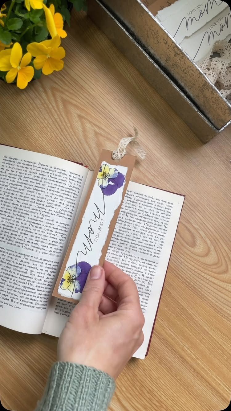 Handmade kraft paper bookmark with purple flowers held inside an open book.