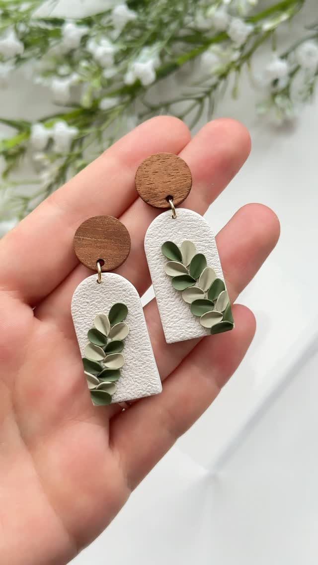 Handmade clay earrings with white arches and green leaves held in a hand.
