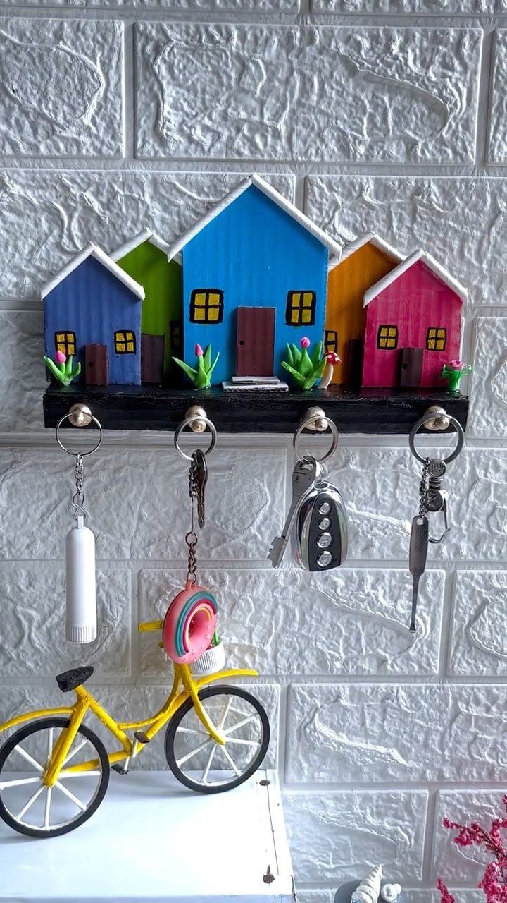 Colorful wooden house-shaped key holder with keys hanging on a white brick wall.
