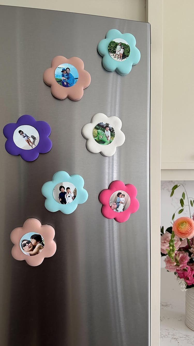 Flower-shaped photo magnets in pastel colors attached to a stainless steel refrigerator door.