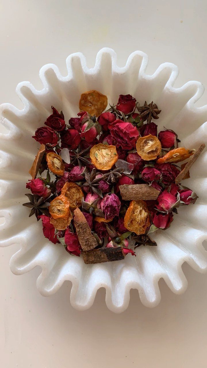Dried rosebuds, star anise, and cinnamon sticks in a white scalloped bowl.
