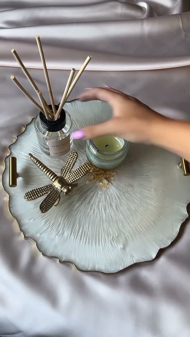 White resin tray with gold edges holding a diffuser, candle, and dragonfly ornament.