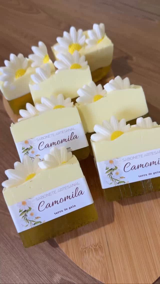 Handmade chamomile soaps with white daisy decorations on a light wooden board.