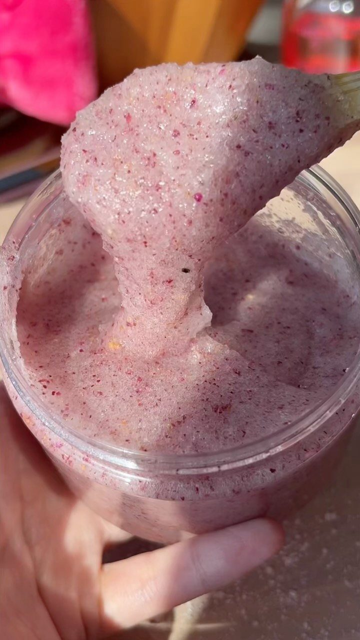 Pink grainy sugar scrub being scooped out of a clear plastic jar