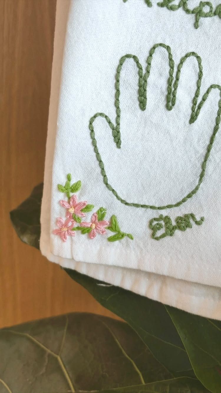 Embroidered white towel with a green hand outline and pink floral details.