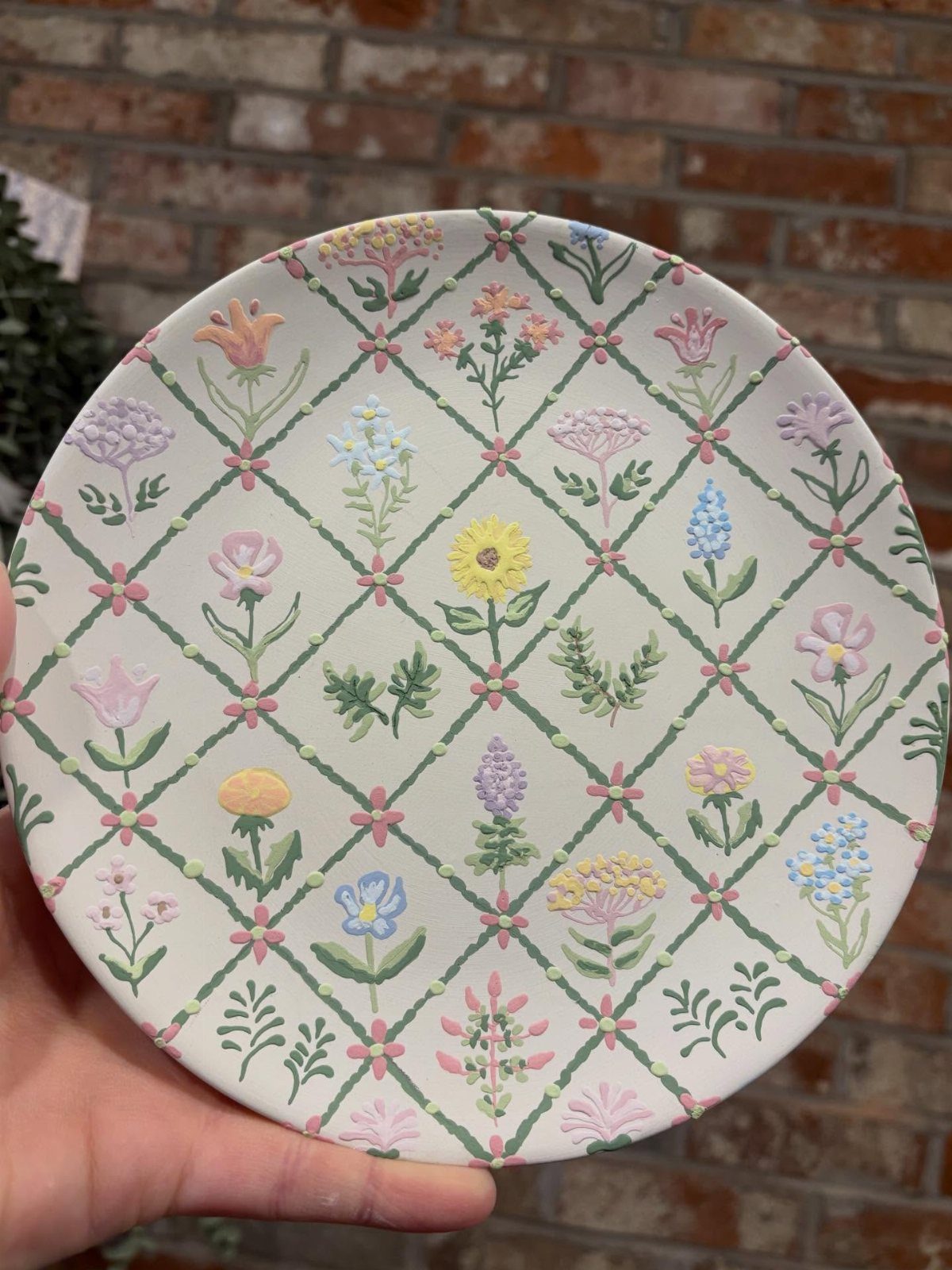 White ceramic plate with hand-painted colorful flowers and a green trellis pattern