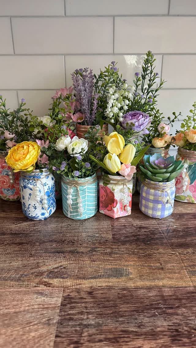 Decorated glass jars filled with colorful artificial flowers on a wooden table