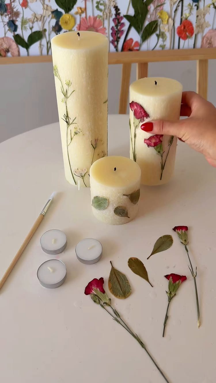Pressed flower decorated pillar candles on a white table with craft supplies
