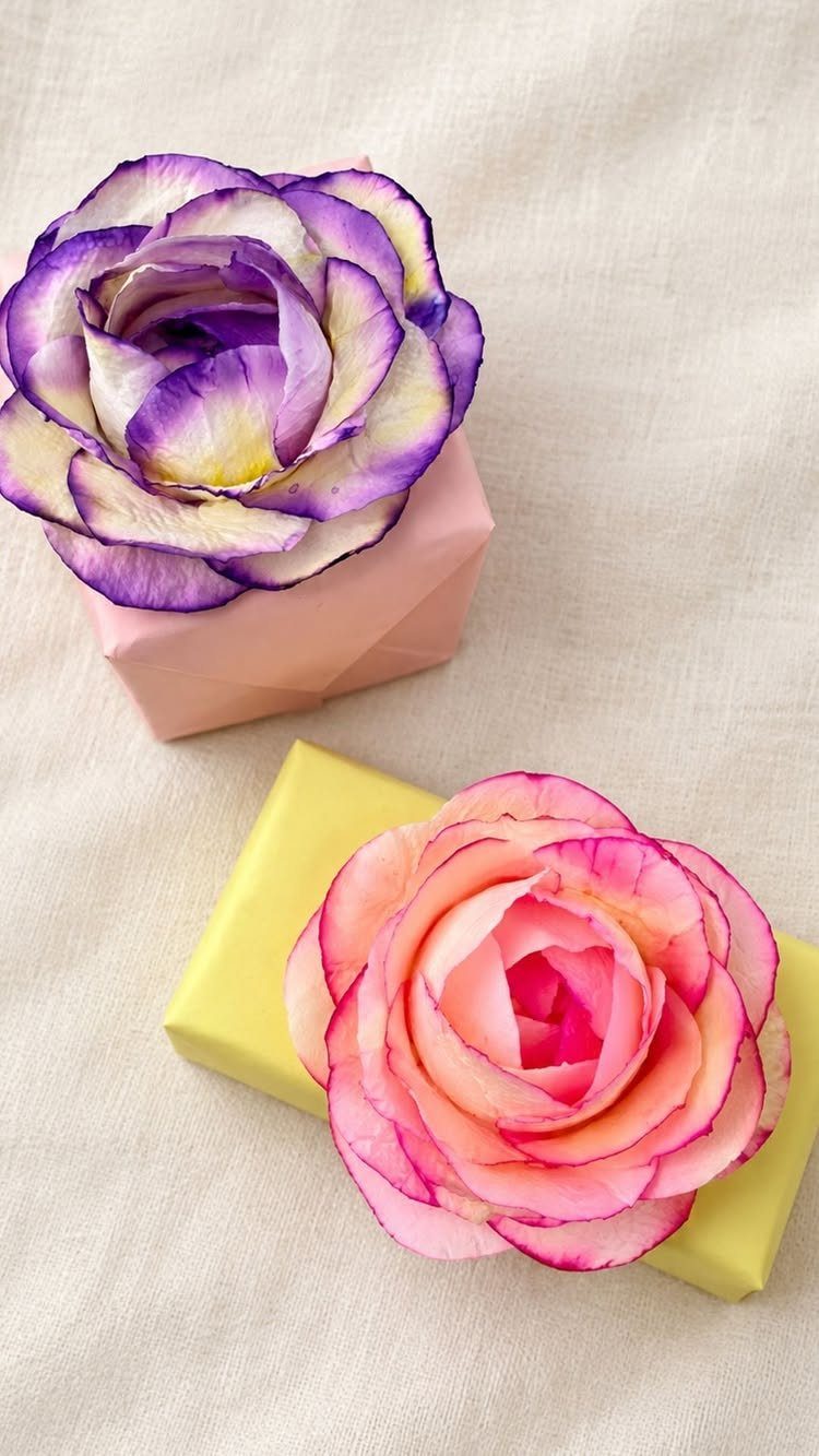 Handmade purple and pink paper roses decorating small wrapped gift boxes on fabric.