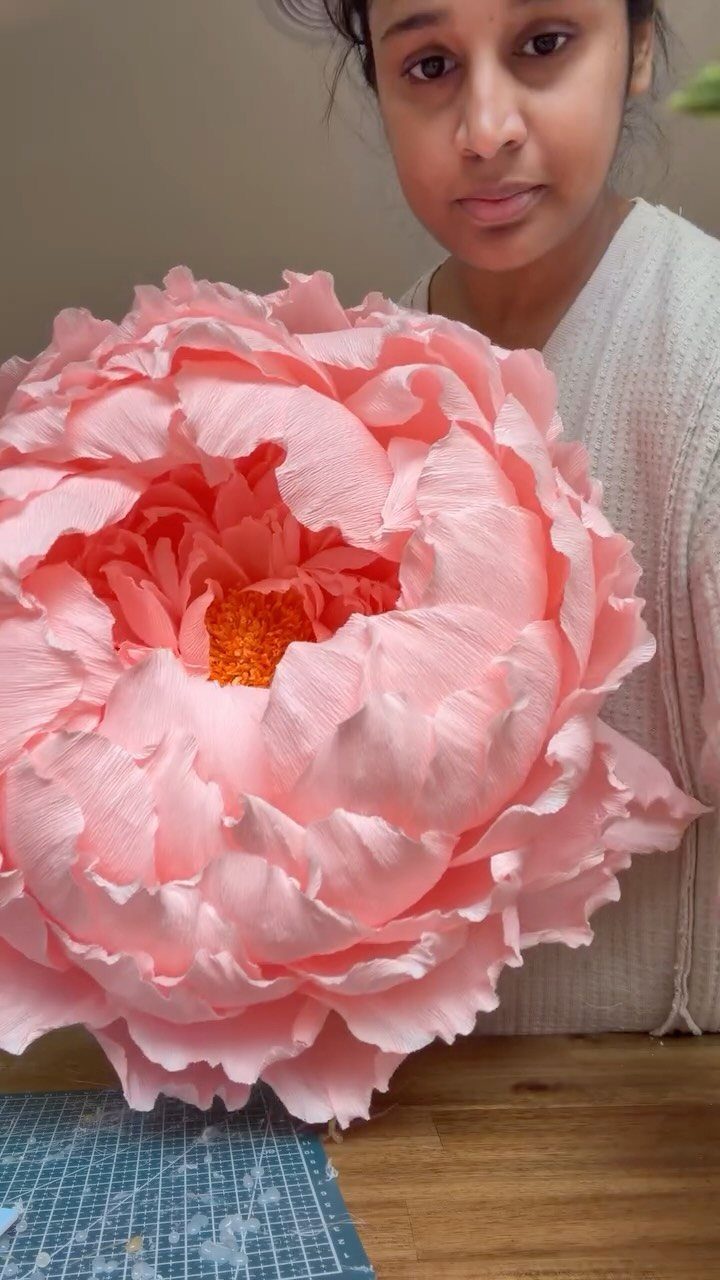 Giant pink crepe paper peony held by a woman over a wooden table.