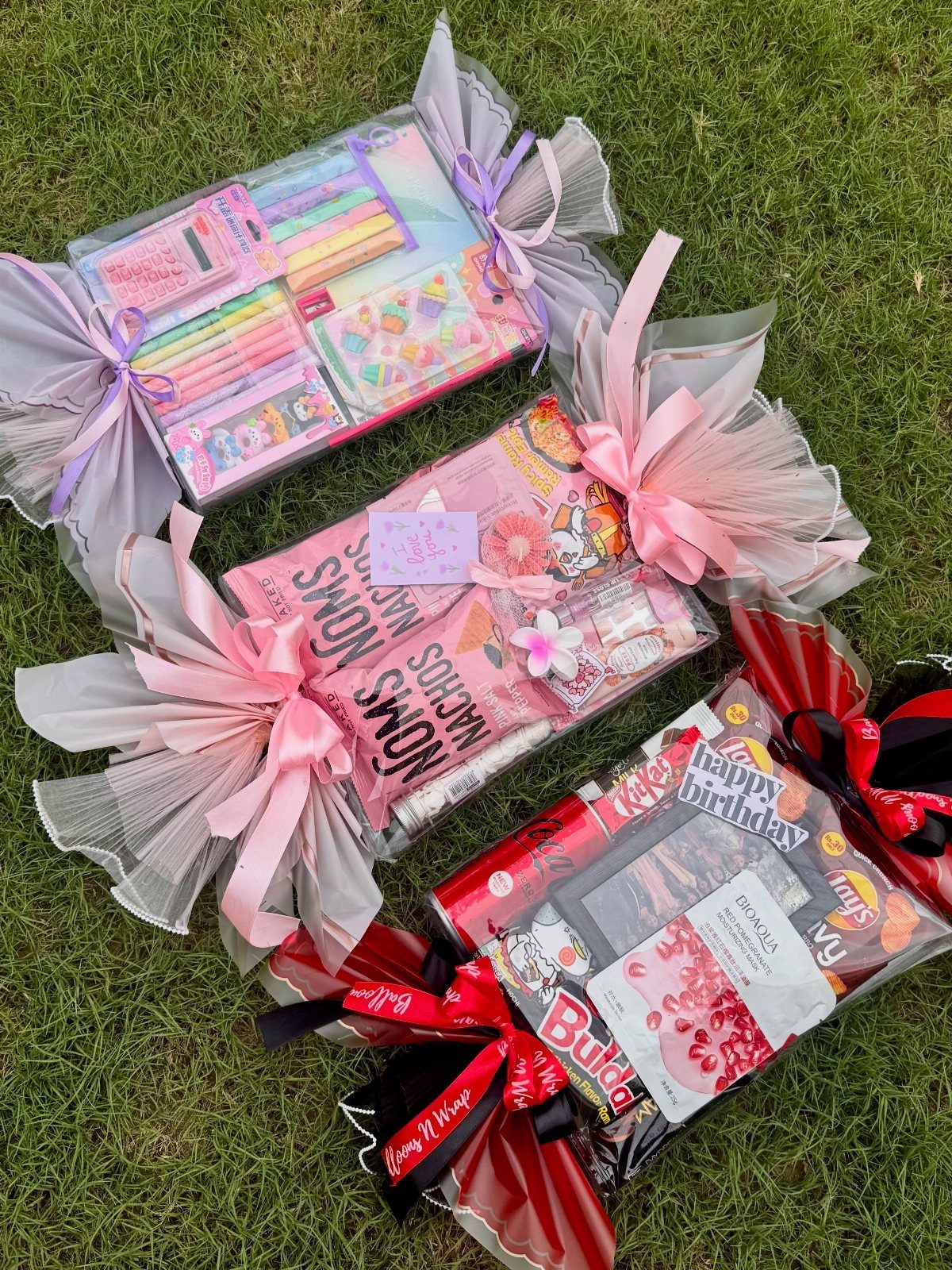 Three cellophane-wrapped gift baskets with large colorful bows resting on green grass.