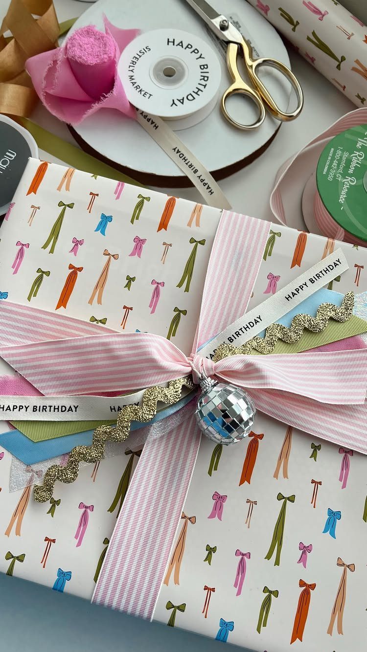 Wrapped gift with tie-patterned paper, pink ribbons, and a tiny disco ball ornament.