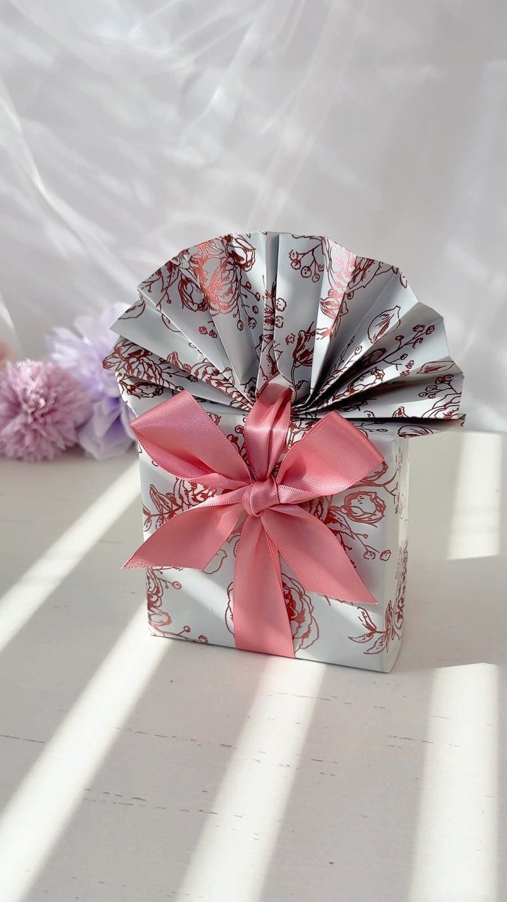 Wrapped gift with red floral paper, pink satin bow, and pleated paper topper.