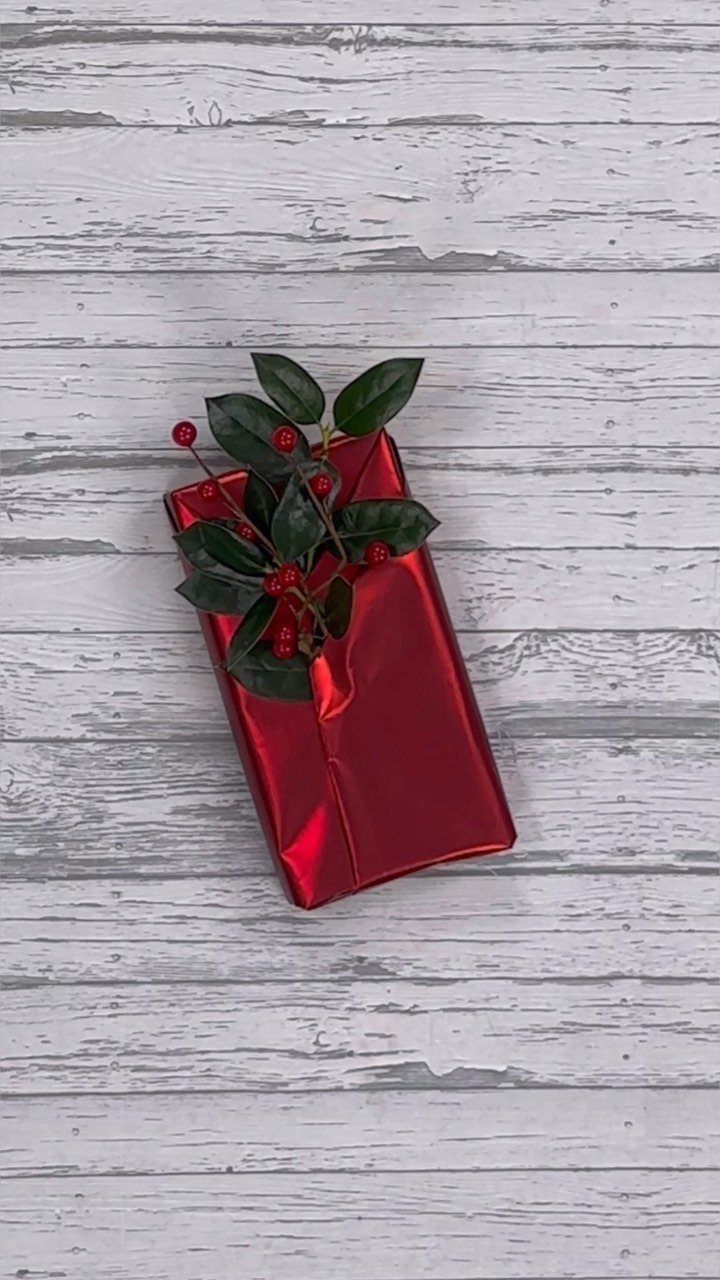 Red metallic wrapped gift with green leaves and berries on white wood