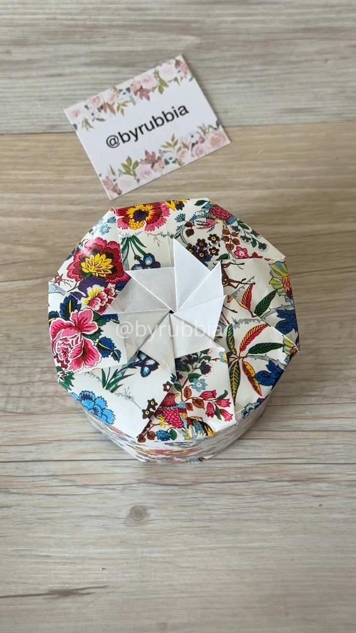 Floral wrapped round gift with a white folded paper star on wooden surface