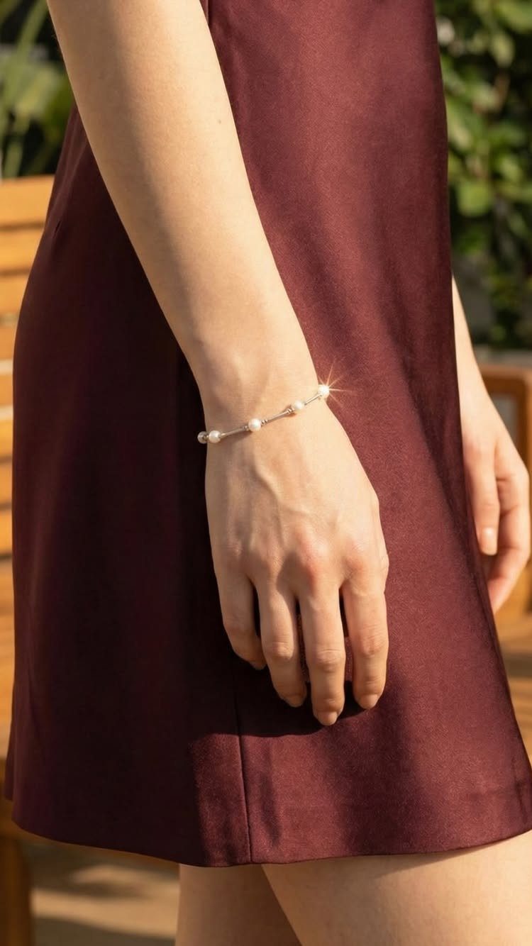 Person in a maroon dress wearing a delicate white pearl bracelet on wrist.