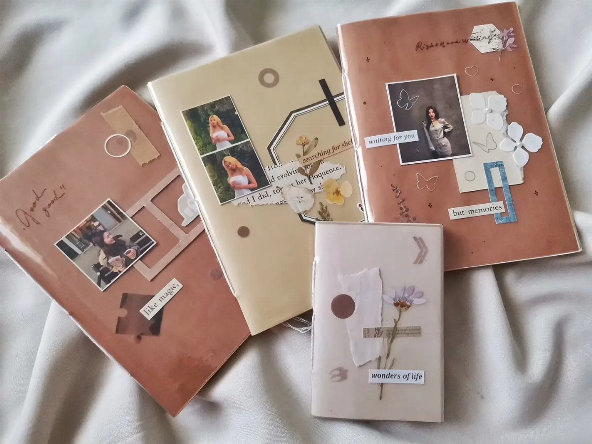Four decorated journals with photos and dried flowers on a white fabric background.
