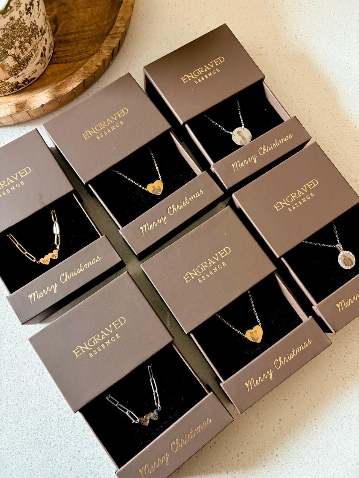 Six engraved necklaces with pendants in brown gift boxes on a white surface.