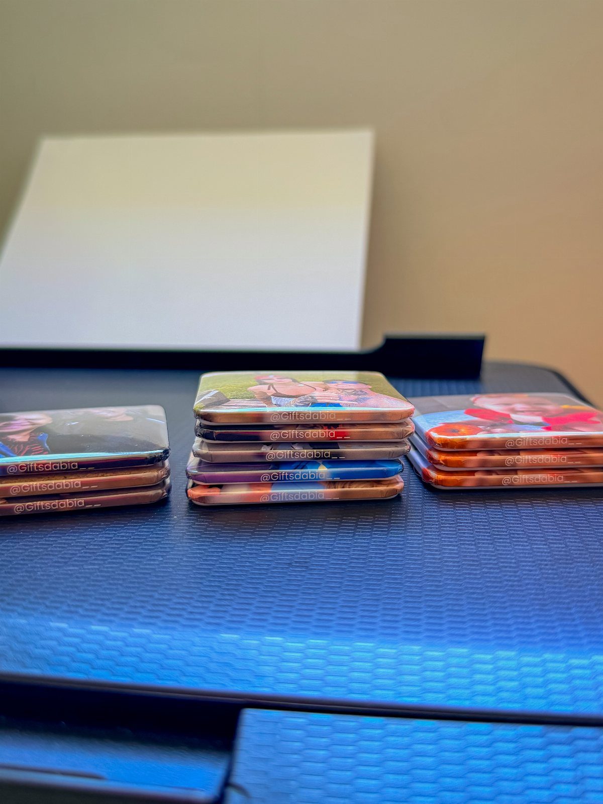 Stacks of square photo coasters with colorful images on a blue surface