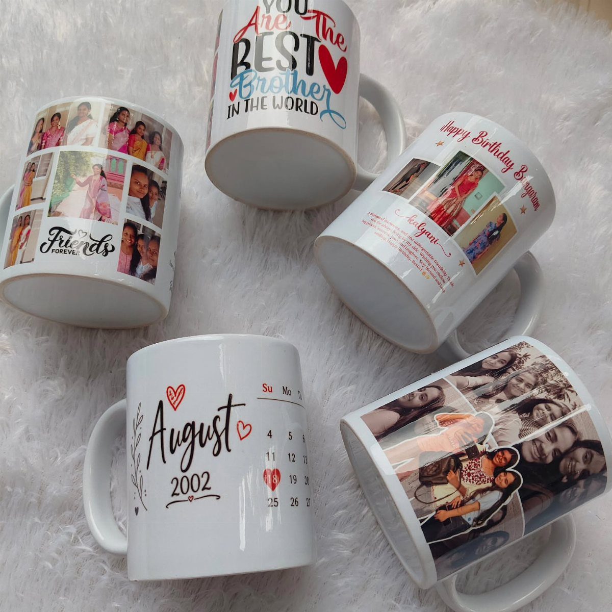 Five personalized white ceramic mugs with photos and text on white fluffy fur.