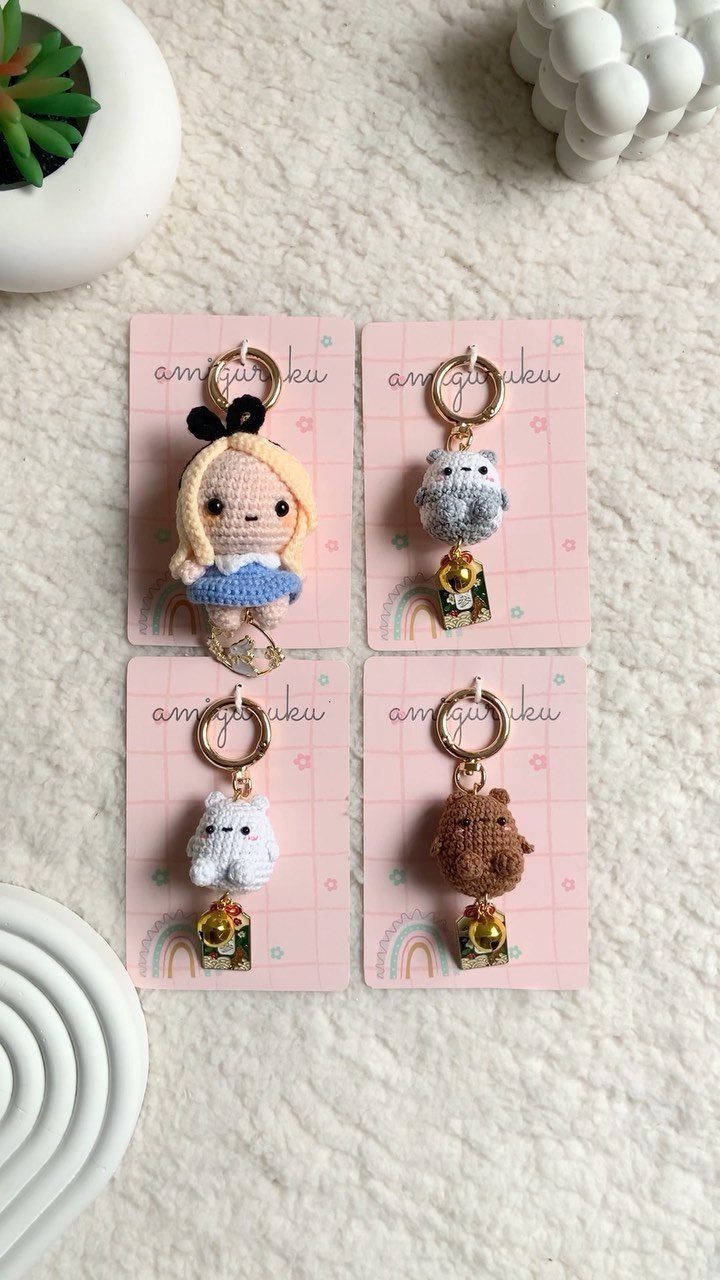 Four crochet keychains of a girl and animals on pink display cards.