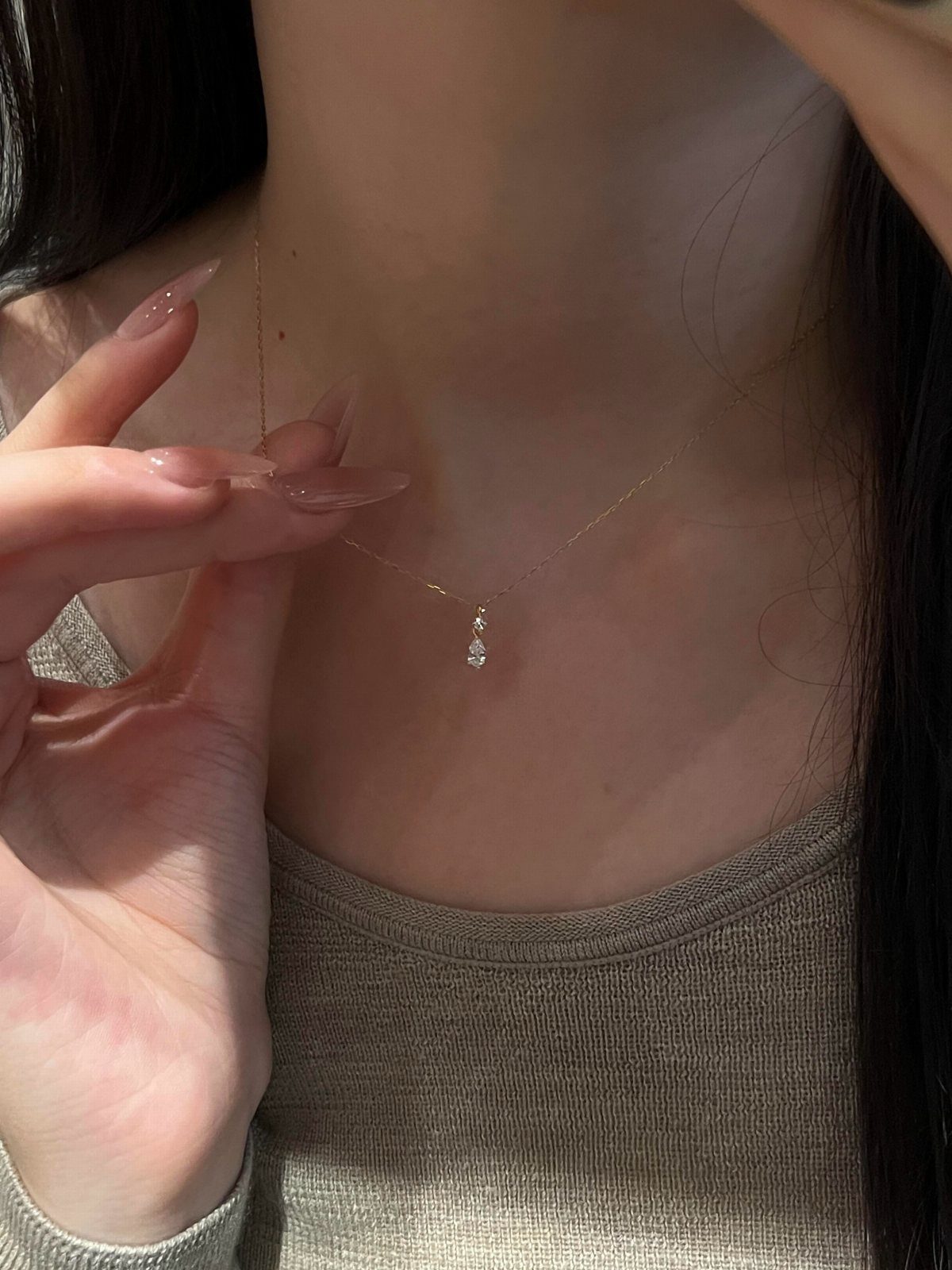 Thin gold chain necklace with a small teardrop diamond pendant worn on a person.