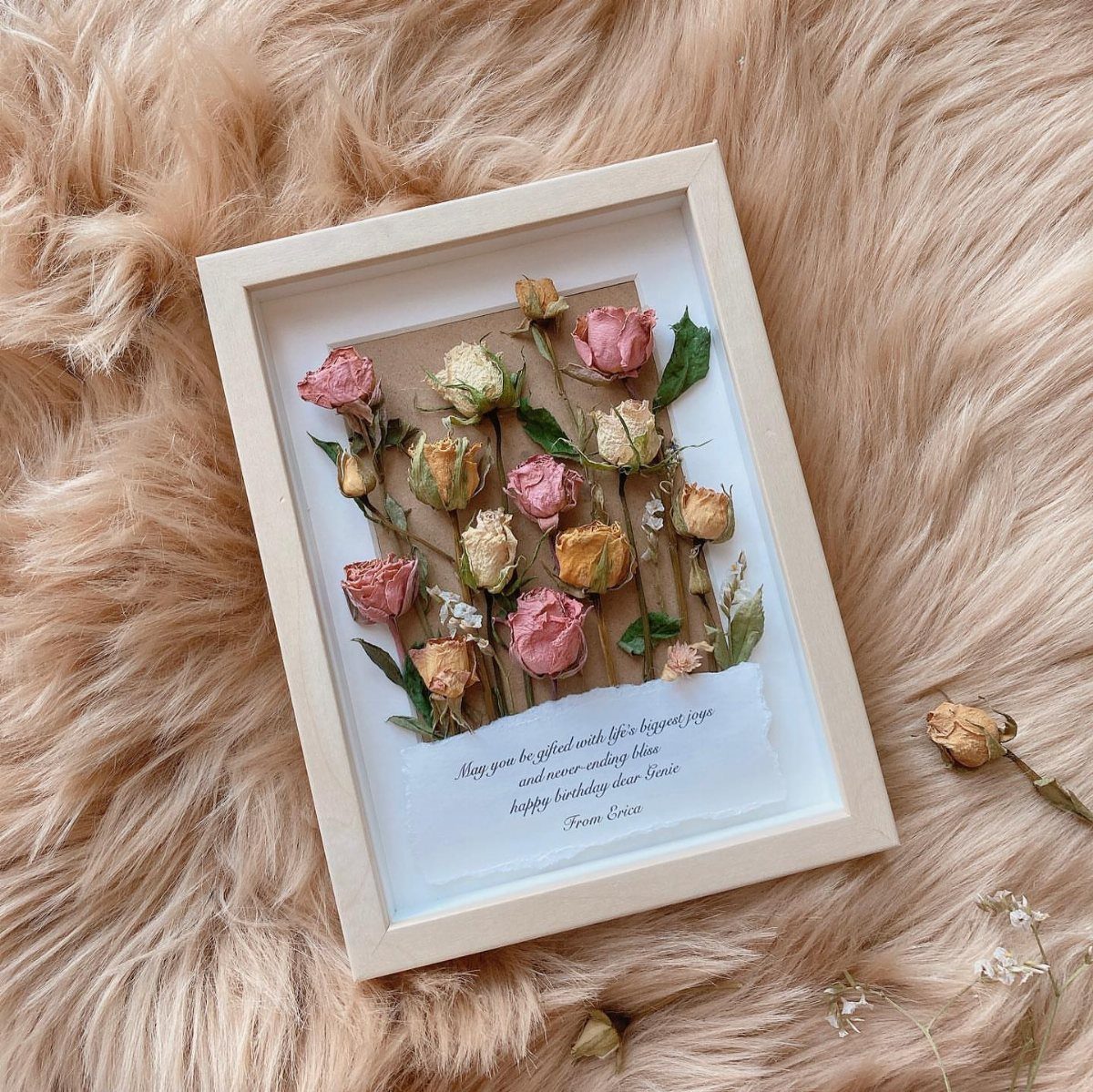 Dried pink and yellow roses framed with a handwritten note on fluffy fur.