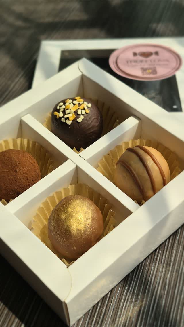 Four assorted chocolate truffles in a white divided gift box on wooden table