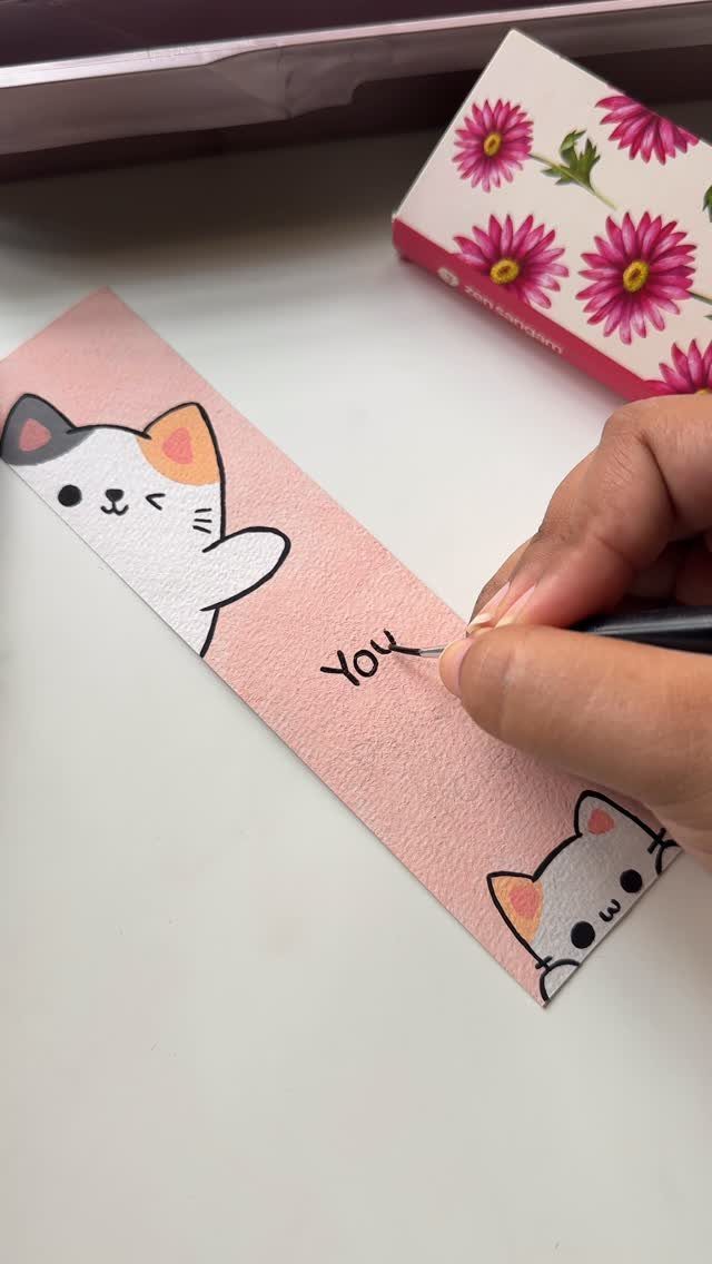 Hand drawing a pink handmade bookmark with cute cartoon cats and text.