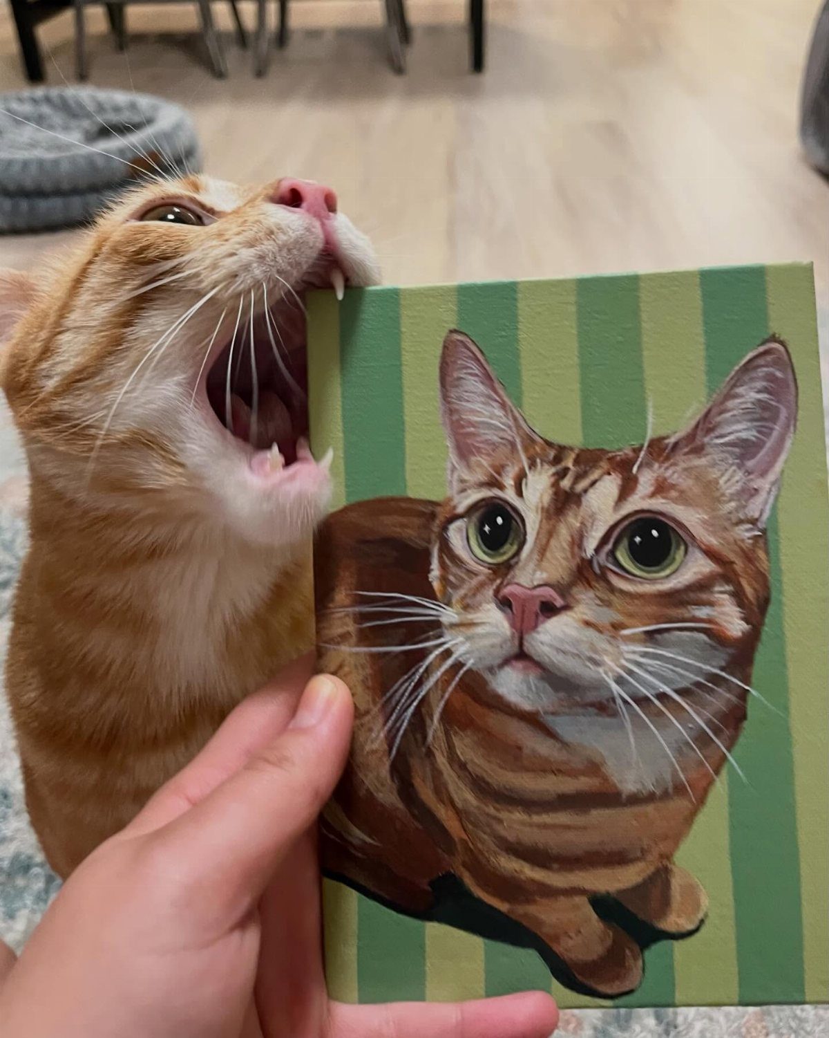 Orange tabby cat biting a custom canvas portrait of itself with green stripes.