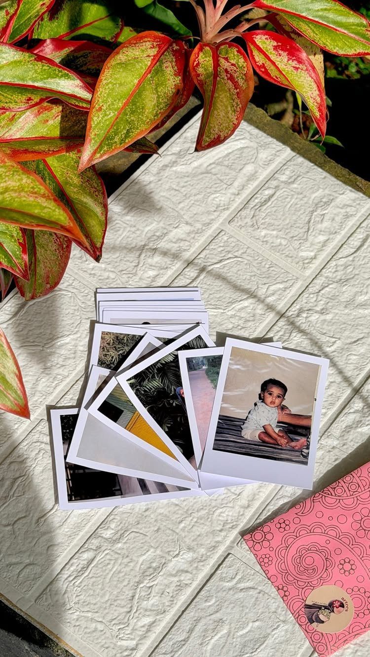 Instant photo prints scattered on a white surface next to a pink notebook.