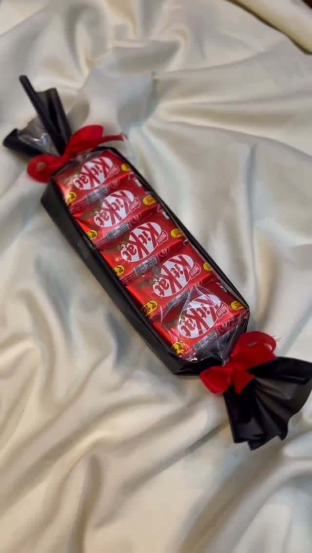 KitKat chocolate bars wrapped in black cellophane with red ribbons on white fabric