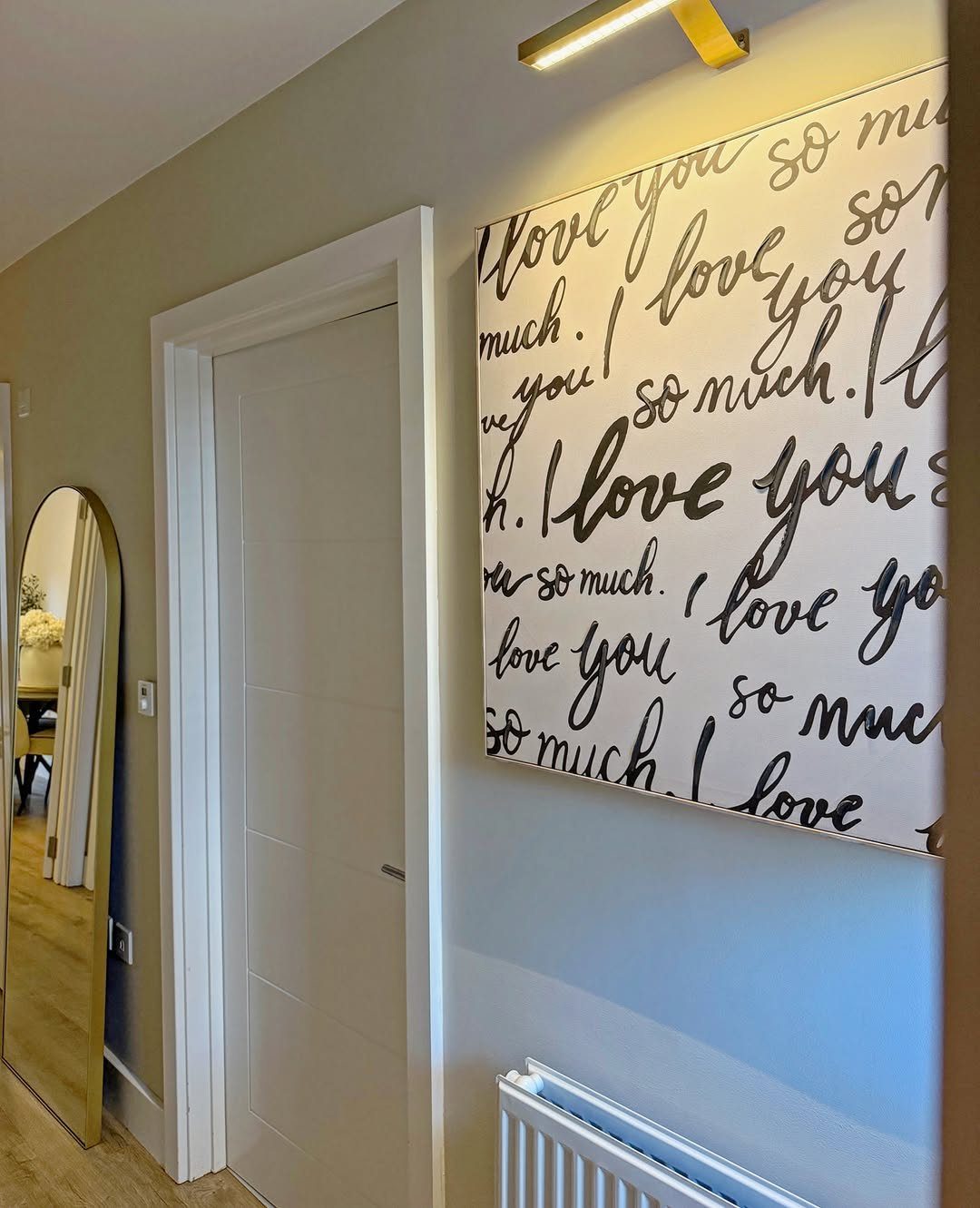 Canvas painting with black cursive love text hanging on a grey wall.