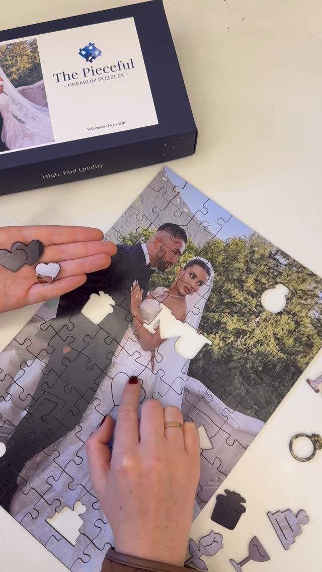 Hands assembling a custom wedding photo jigsaw puzzle on a white surface.
