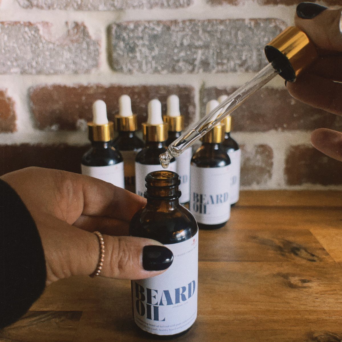 Hands filling a brown glass bottle labeled Beard Oil using a glass dropper.