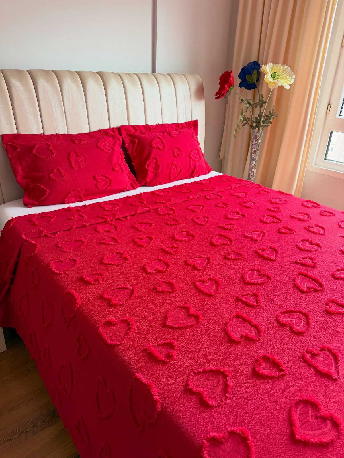 Red textured blanket and pillows with raised heart patterns on a bed
