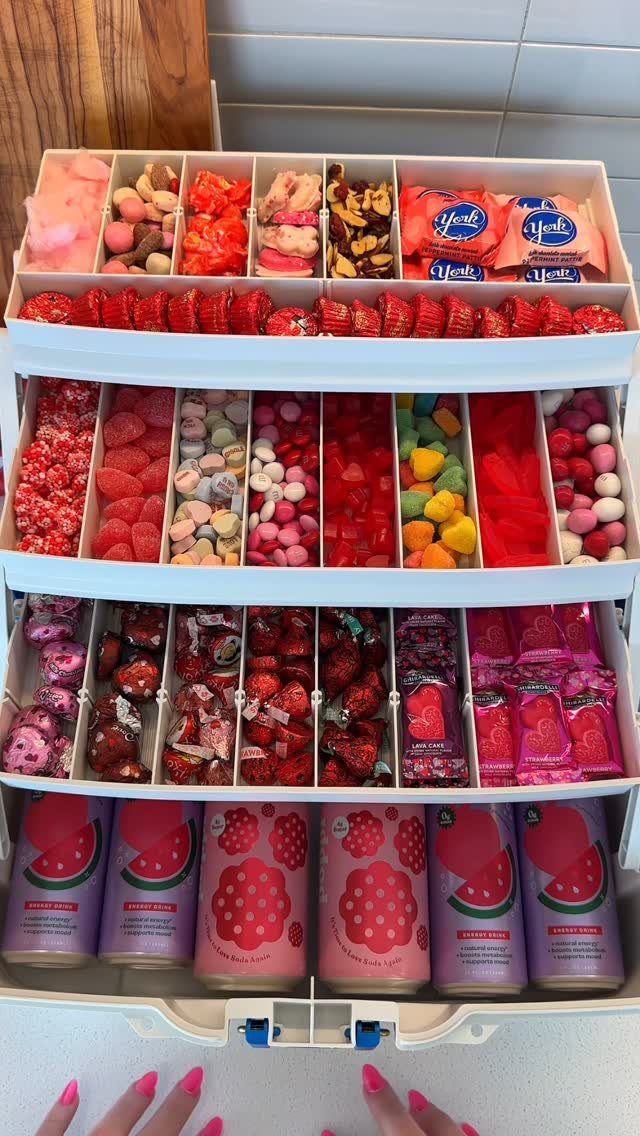 White tackle box filled with red and pink candies and pink beverage cans.