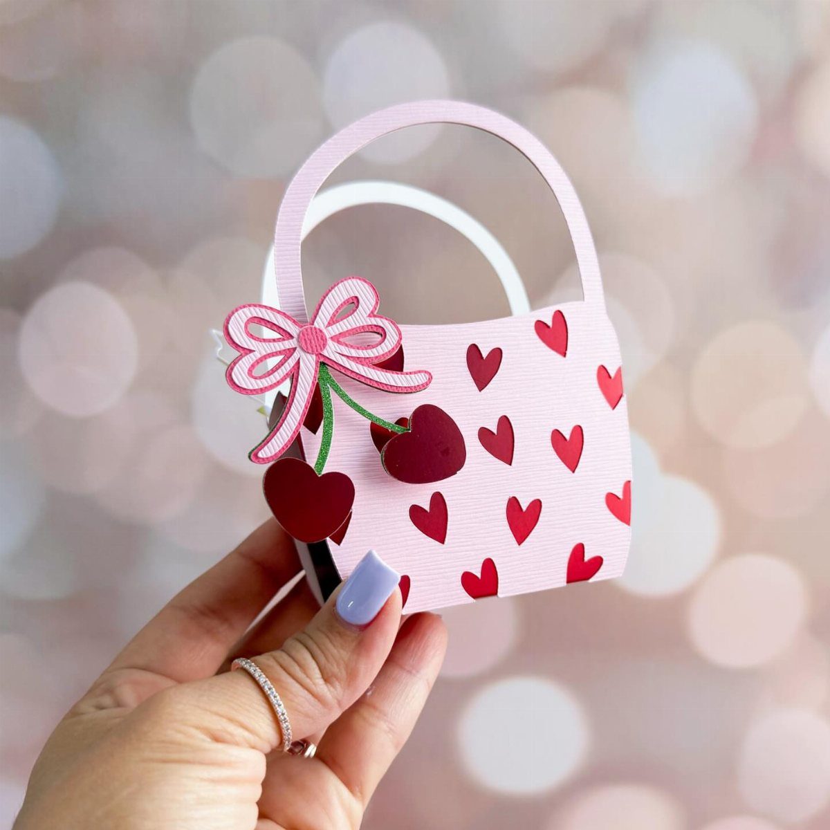Small pink paper gift bag with red hearts and a bow held by hand.