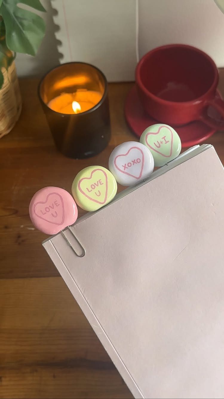 Pastel heart-shaped clay bookmarks with romantic messages clipped to a white book.
