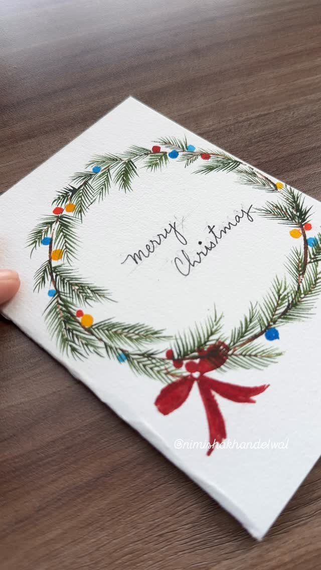 Watercolor Christmas card featuring a green evergreen wreath with a red bow.