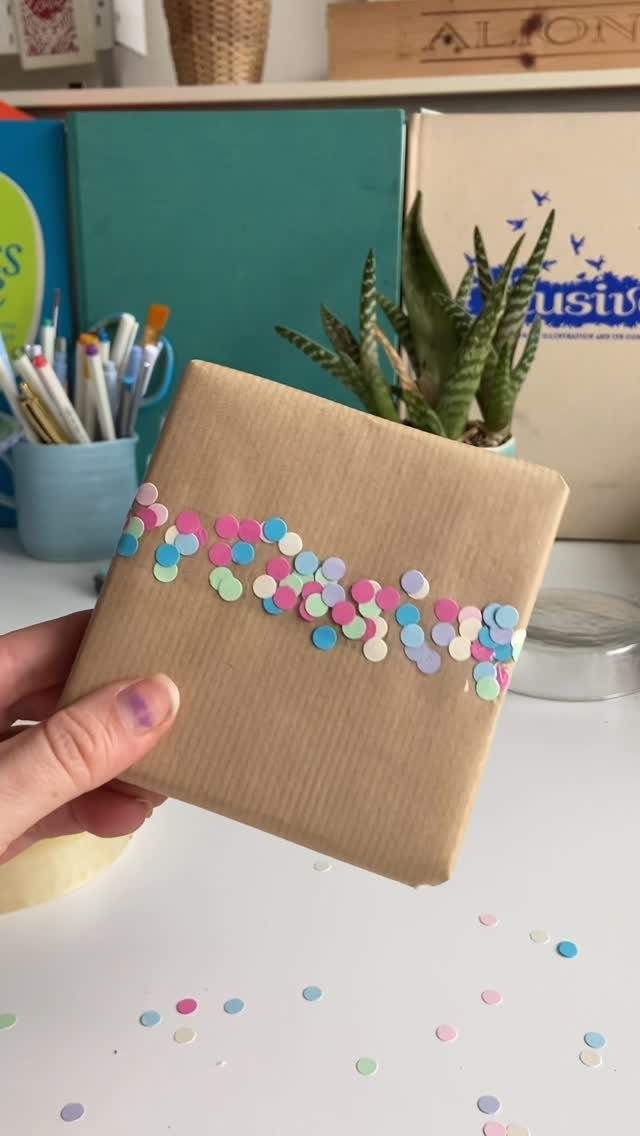 Brown paper wrapped gift decorated with a line of colorful pastel confetti circles.