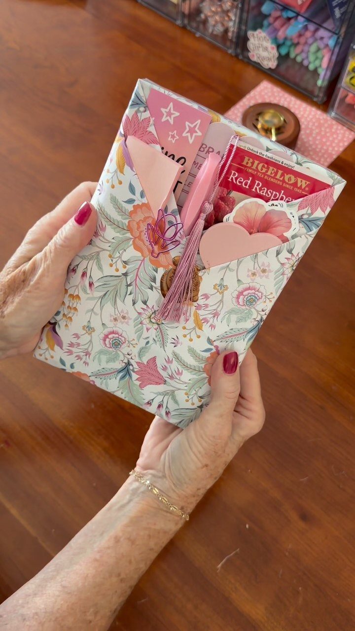 Floral paper envelope held by hands containing tea and pink paper hearts.