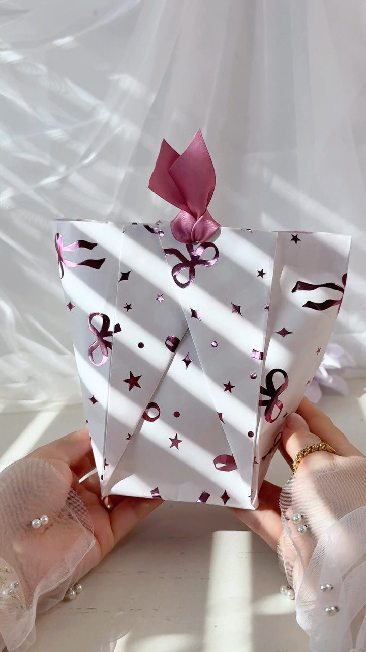 Small white gift bag with purple patterns and ribbon held by two hands.