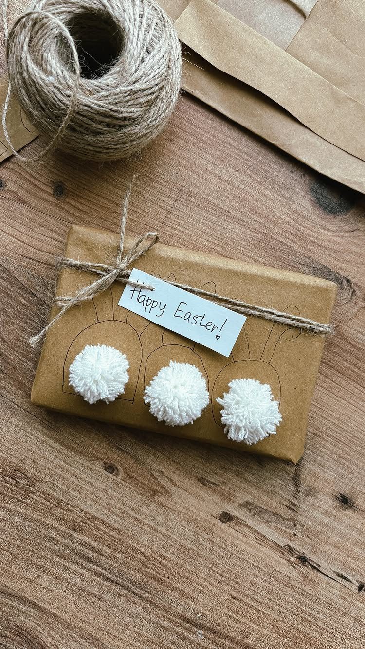 Brown paper wrapped gift with twine and three white pom poms on wood.