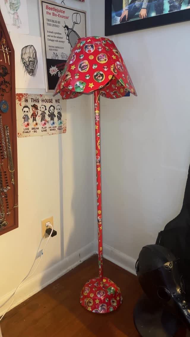 Floor lamp wrapped in red patterned gift paper standing against a white wall